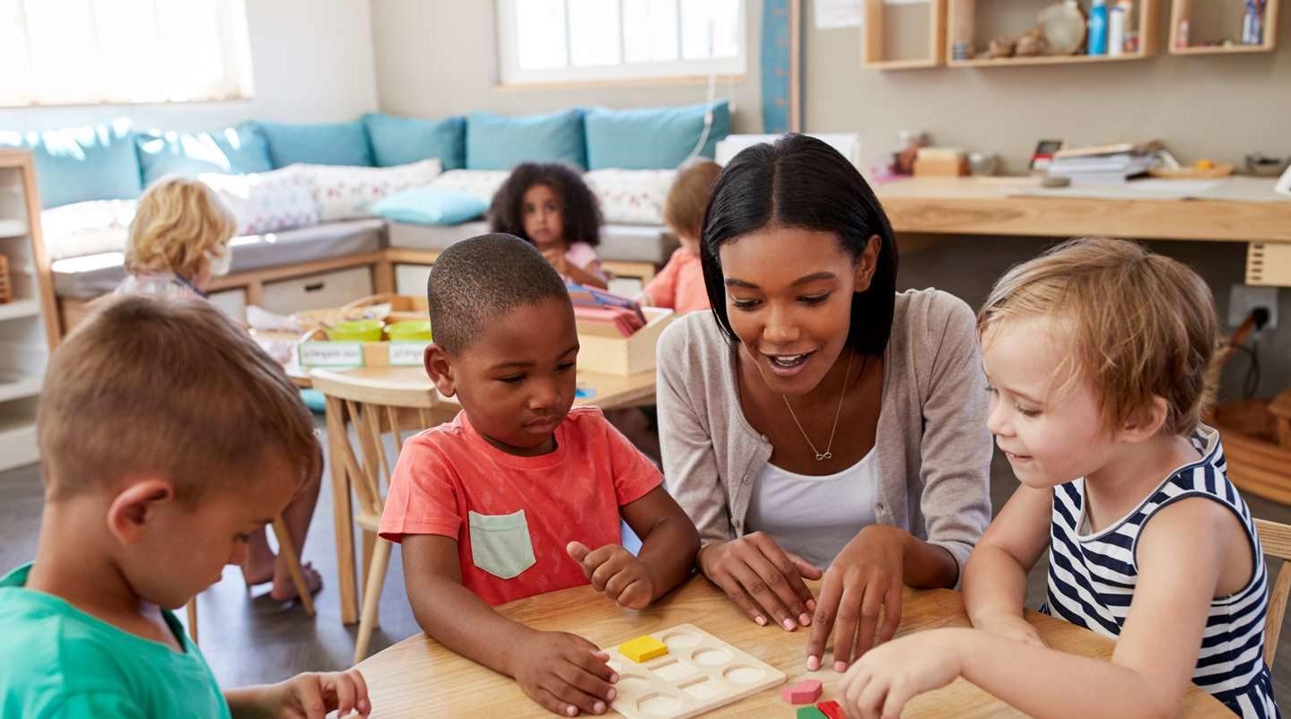 Teacher helping children learn to put blocks into a puzzle.